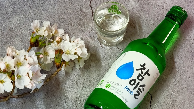 Green bottle of soju, with a shot glass and some decorative cherry blossoms